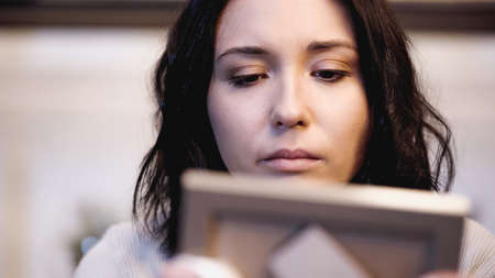 close up view of upset woman looking at photo frame photo frame at homeの写真素材