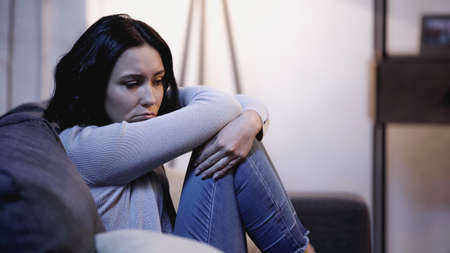 depressed woman sitting on sofa in self hug pose at homeの写真素材