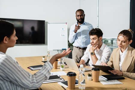 thoughtful african american businessman pointing with finger during meeting with coworkers