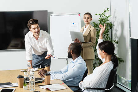 excited businessman pointing with pen near interracial business team in conference room