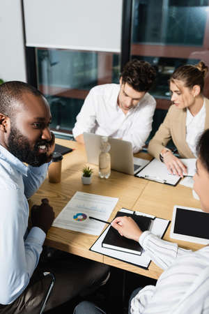 african american businesswoman pointing at infographics during meeting with colleagues