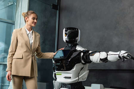 happy businesswoman touching humanoid robot in officeの写真素材