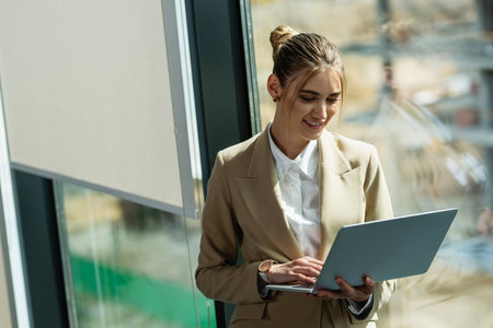 smiling woman using laptop near window in officeの写真素材