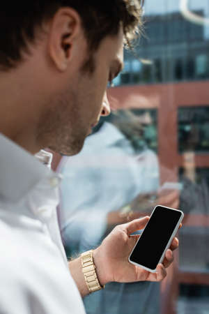 businessman on blurred foreground holding smartphone with blank screen near windowの写真素材
