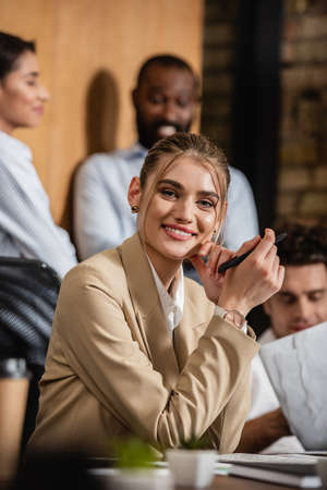 joyful businesswoman looking at camera near blurred interracial business partnersの写真素材