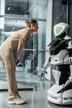 full length view of young businesswoman looking at humanoid robot in officeの写真素材