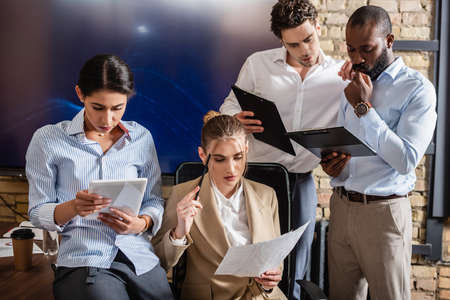 thoughtful interracial business people working with digital tablet and documents in conference room