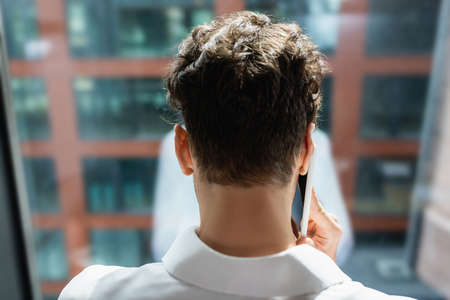 back view of young businessman talking on mobile phone near windowの写真素材