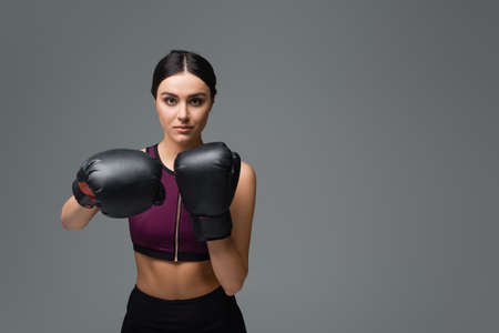 pretty sportswoman looking at camera while boxing isolated on grayの写真素材
