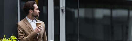 pensive businessman in formal wear holding paper cup near building, bannerの写真素材