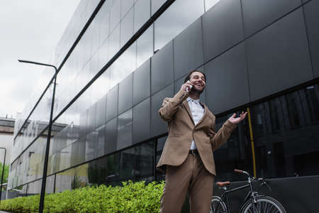 low angle view of happy businessman talking on cellphone near building