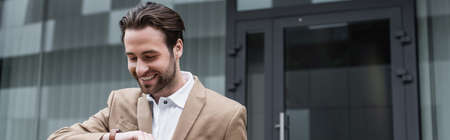 happy bearded businessman in suit looking at wristwatch, banner