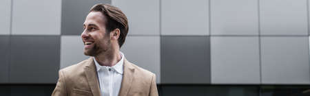 cheerful businessman looking away near concrete building outside, bannerの写真素材