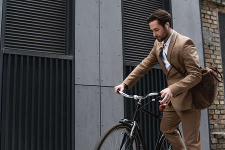 bearded businessman in earphones riding bicycle outside