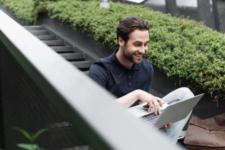 happy man smiling while using laptop outside