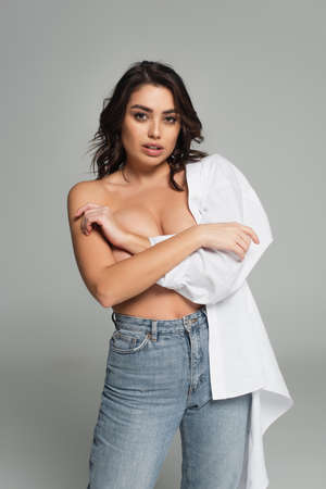 Brunette woman in white shirt covering breast isolated on gray