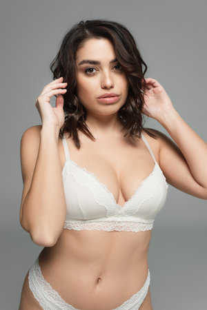 Pretty brunette woman in lingerie looking at camera isolated on grayの写真素材