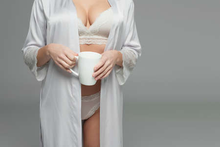 Cropped view of woman in underwear and satin robe holding white cup isolated on grayの写真素材