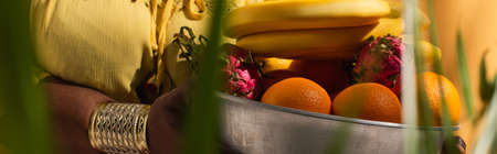 cropped view of metal bowl with fruits in hands of african american woman on orange, bannerの写真素材