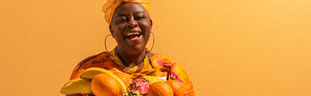 smiling middle aged african american woman with exotic fruits on orange, banner