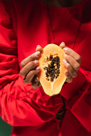 close up view of half cut of papaya in hands of young african american woman in red blouse