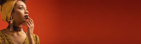 young african american woman with lipstick touching lips with finger on red, bannerの写真素材