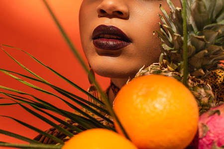 close up view of fruits and lips with lipstick on face of young african american woman on orange