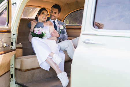 Smiling groom embracing bride in vintage carの写真素材