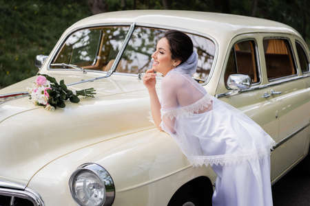Side view of happy bride standing near vintage car outdoorsの写真素材