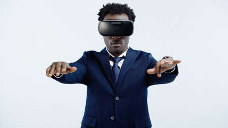 curly african american businessman in suit and vr headset standing with outstretched hands isolated on blueの写真素材