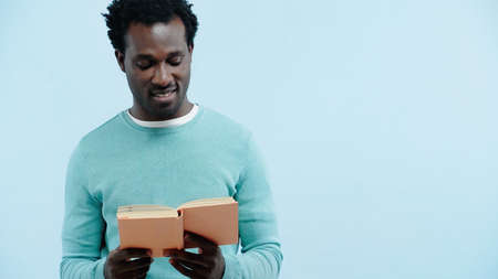 happy african american man reading book isolated on blue