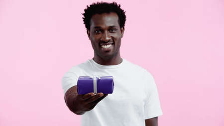 cheerful african american man in white t-shirt holding wrapped present isolated on pinkの写真素材