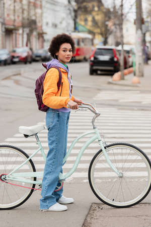 Young african american woman standing near bike on road on urban streetの写真素材
