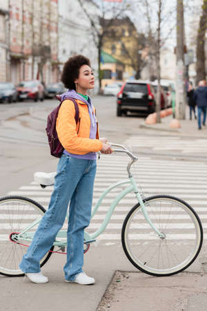 Young african american woman standing near bicycle and crosswalk outdoorsの写真素材