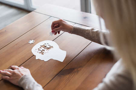Blurred woman folding jigsaw on wooden tableの写真素材