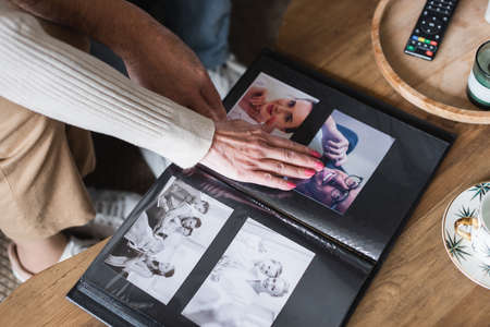 Cropped view of senior couple sitting near photo album and cup on tableの写真素材