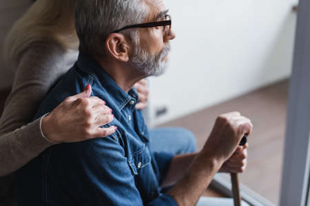 Side view of woman on blurred background hugging husband with crutch at homeの写真素材
