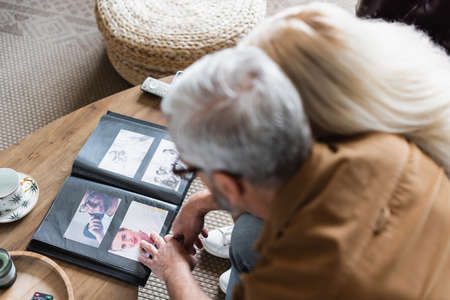 Overhead view of blurred elderly couple sitting near photos in album on tableの写真素材