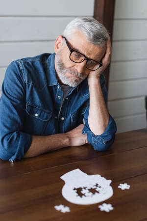 Sad senior man with dementia looking at jigsaw on tableの写真素材