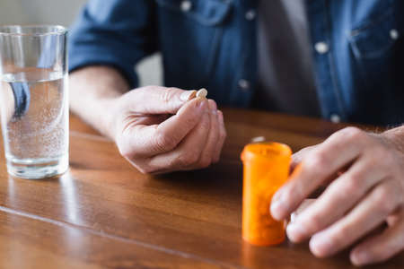 Cropped view of senior man holding pill near jar and glass of waterの写真素材