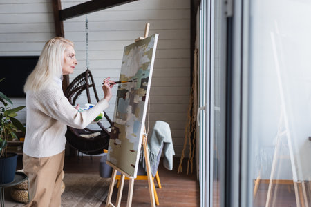 Side view of senior woman painting on canvas at homeの写真素材