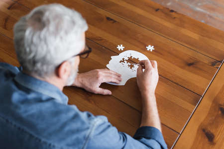 Overhead view of senior man on blurred foreground folding puzzle on tableの写真素材