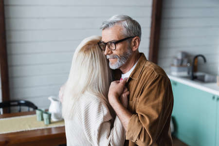 Senior man in eyeglasses holding hand of wife at homeの写真素材