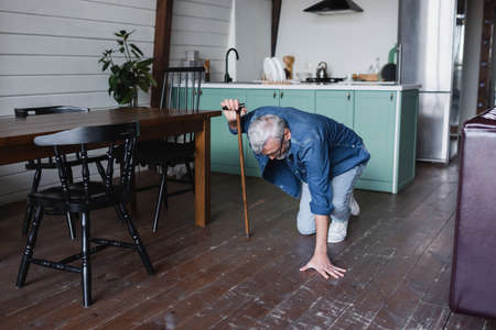 Elderly man with crutch falling on floor at homeの写真素材