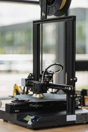 3D printer creating plastic model on table near window in modern officeの写真素材