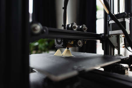 close up view of 3D printer creating plastic model near produced figure on table in modern officeの写真素材