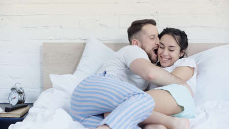 happy bearded man with open mouth hugging cheerful girlfriend with braids