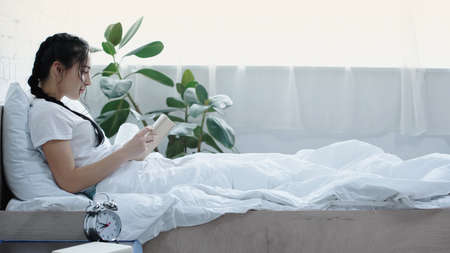 side view of bearded woman reading book in bedの写真素材