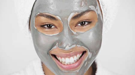 Close up view of happy african american woman in clay mask on face isolated on gray