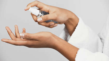 Cropped view of african american woman in bathrobe using hand sanitizer isolated on gray
